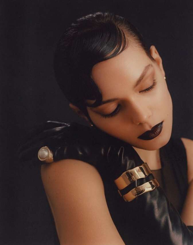 Close-up portrait of a woman with dark finger waves, dark lipstick, black leather gloves, pearl ring, and gold cuffs by Julia Sariy.