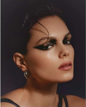 Close-up portrait of a woman with dramatic winged black eyeliner and a silver hoop earring against a dark backdrop