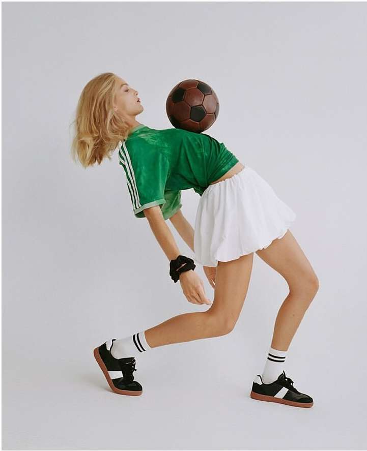 Young woman in athletic pose with a soccer ball balanced on her back. She is wearing a sporty outfit with striped socks and sneakers.