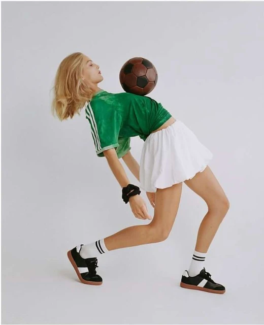 Young woman in athletic pose with a soccer ball balanced on her back. She is wearing a sporty outfit with striped socks and sneakers.