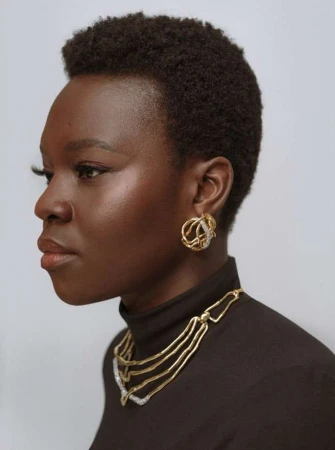 Profile portrait of a Black woman with short afro hair wearing gold statement earrings and necklace by Julia Sariy.