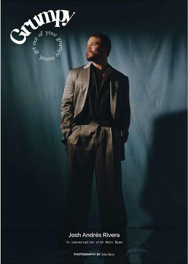 Portrait of Josh Andrés Rivera on the cover of Grumpy magazine, wearing a grey suit against a teal textured backdrop in studio lighting.