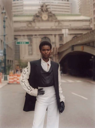 Fashion shot of a Black woman in black and white business-casual attire, striking a pose on a city street with buildings in background.
