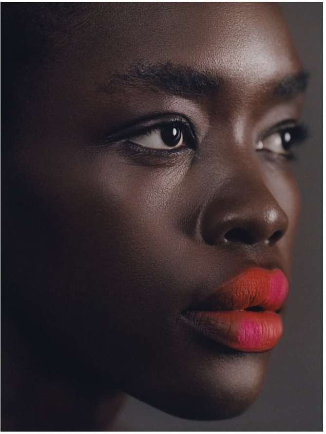 Close-up portrait of a Black woman with bold orange and pink lipstick photographed by Julia Sariy