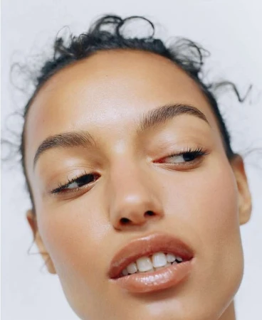 Close-up portrait of a tanned adult female with glossy lips and minimal eye makeup against a plain white background.