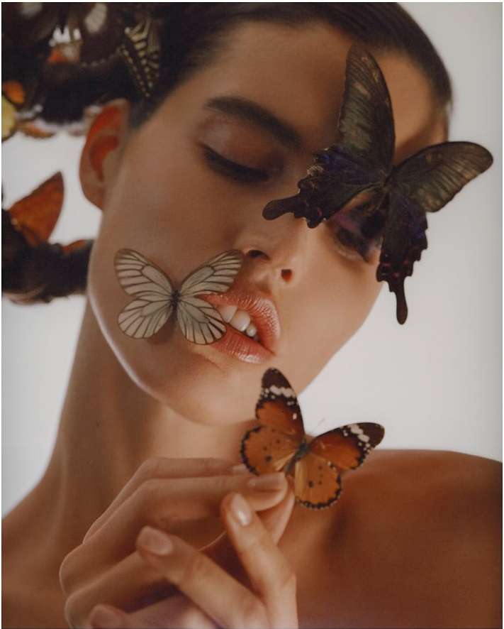 Close-up portrait of a woman with multiple butterflies resting on her face and hands by Julia Sariy