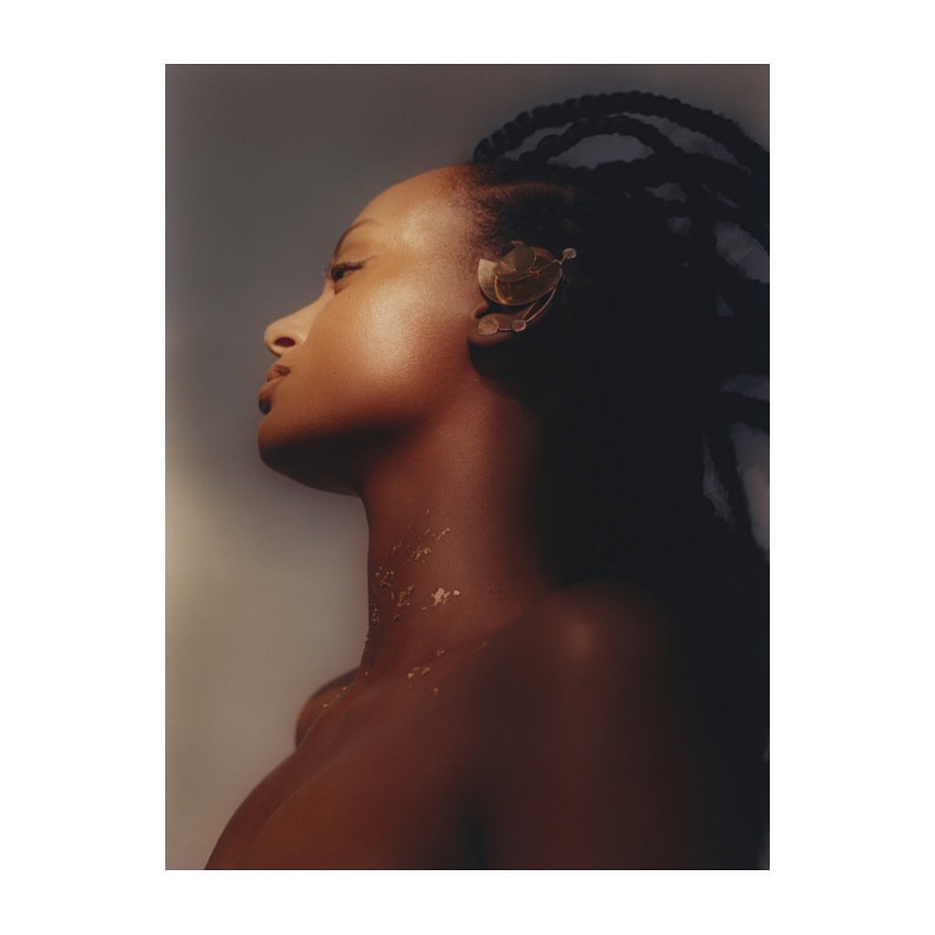 Striking portrait of an African-American woman with braided hair, adorned with a gold ear cuff, looking upwards against a gradient background.