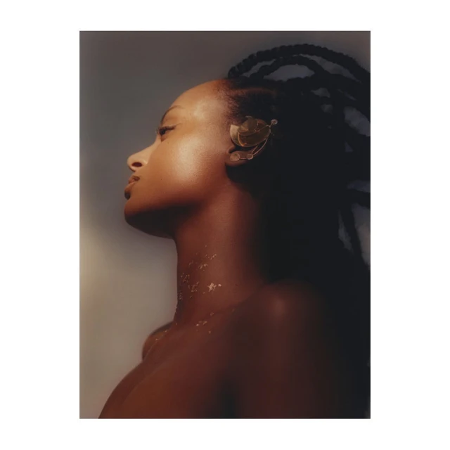 Striking portrait of an African-American woman with braided hair, adorned with a gold ear cuff, looking upwards against a gradient background.