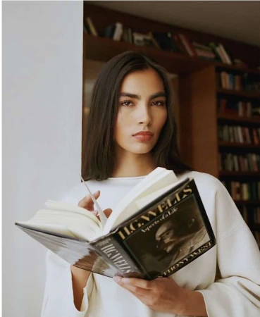 Woman holding open book in front of a bookshelf in a portrait photograph by Julia Sariy