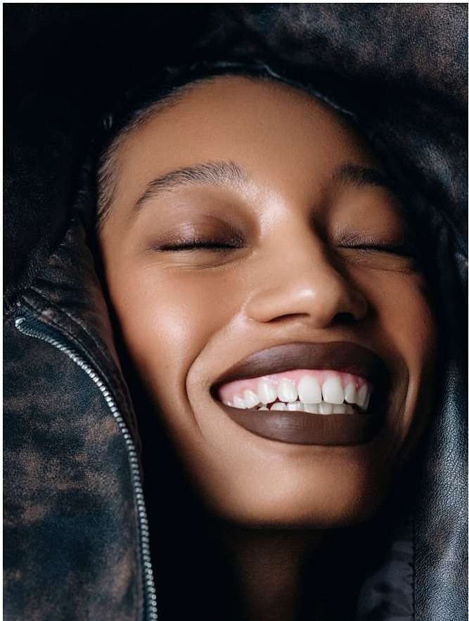 Close-up portrait of a smiling African-American woman with closed eyes, wearing a dark jacket, showcasing beauty and fashion.