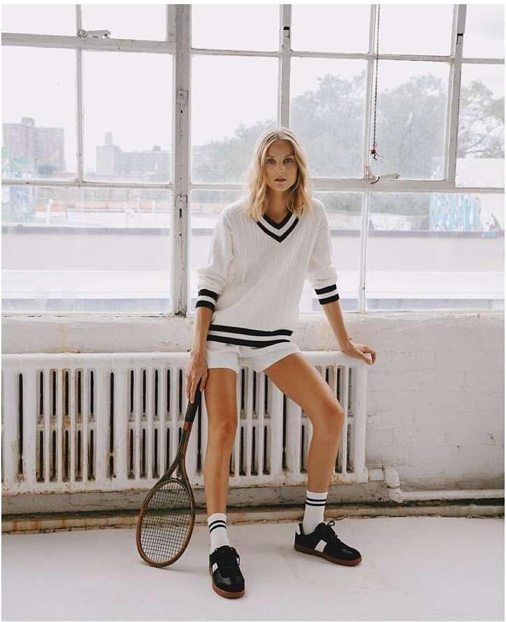 Blonde woman in a white tennis sweater and shorts holding a racket by Julia Sariy