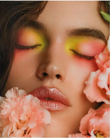 Close up portrait of a woman with vibrant yellow and pink eyeshadow framed by pale pink flowers.