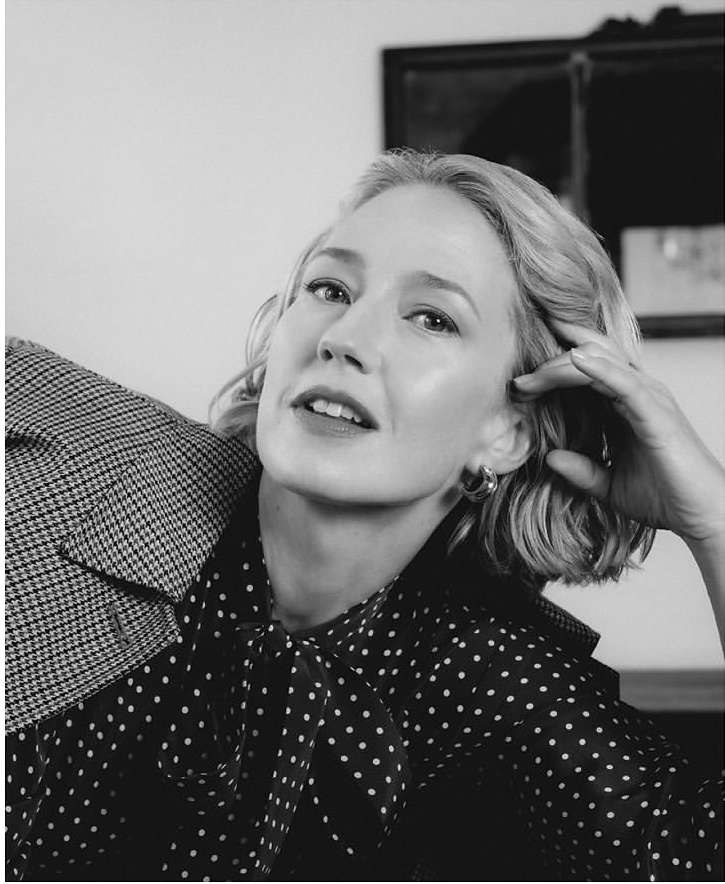 Black and white portrait of a fair-skinned woman with short, wavy blonde hair in a polka dot top and holding a herringbone jacket.