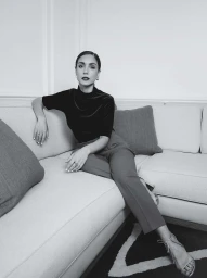 Woman in dark high-neck top and trousers seated on a white sofa in a light interior by Julia Sariy