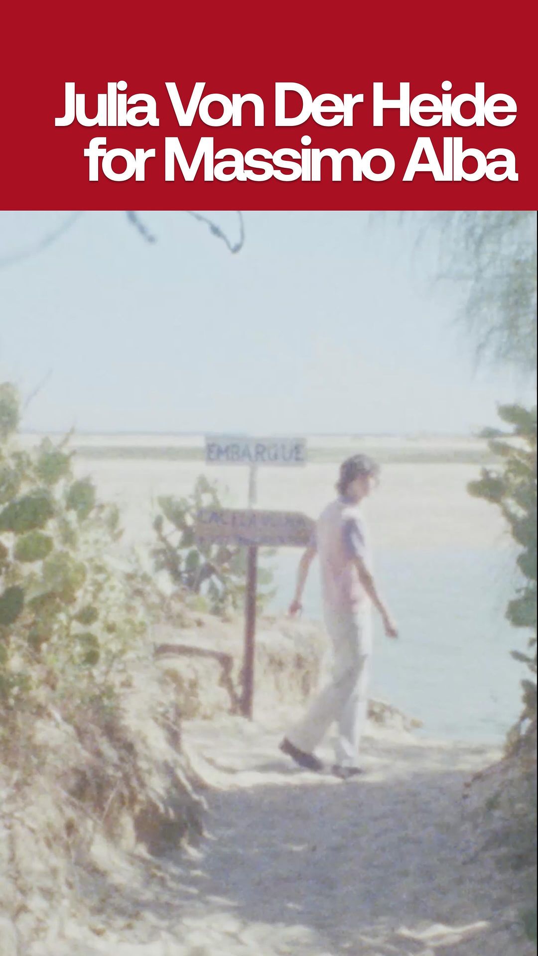 Person walking on sandy path towards the sea with 'Embarque' sign in vintage-style outdoor shot, under bright sunlight.