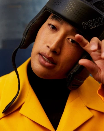 Close-up studio portrait of an Asian adult male wearing a protective boxing headgear and a yellow jacket, with blurred background.