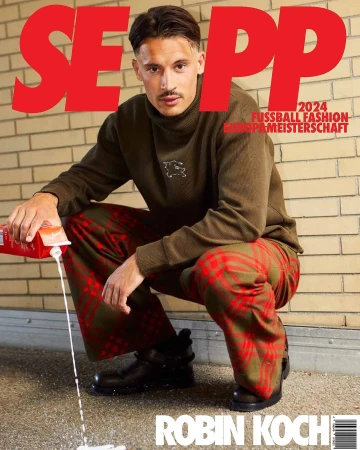 Magazine cover featuring Robin Koch in casualwear, squatting and pouring milk from a carton, with bold red text. Indoor studio setting.
