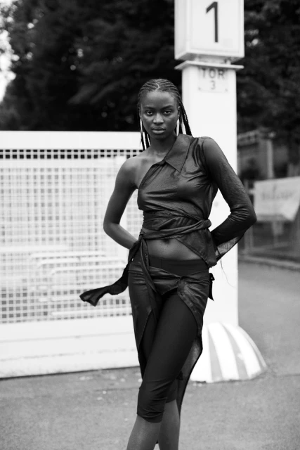 A stunning black and white portrait of a young African woman in a fashionable, avant-garde black outfit, striking a confident pose outdoors.