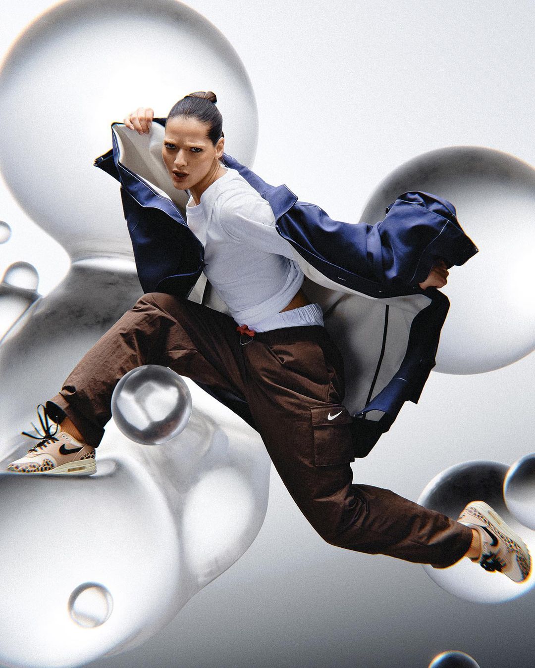 Athletic woman in mid-air wearing athletic gear and sneakers against a light grey background with reflective transparent spheres.
