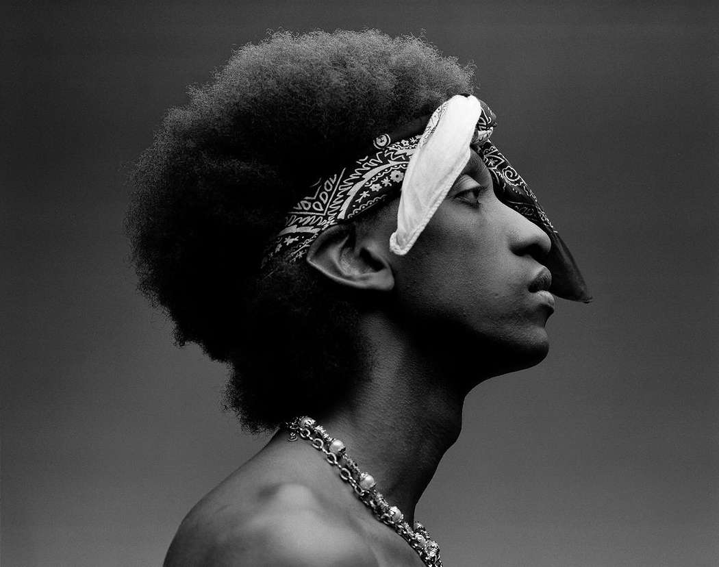 Monochrome portrait of a bare-chested man with an afro and paisley bandana against a gray background, shot in profile view.