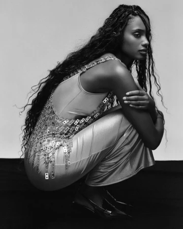 Black and white portrait of a black woman with braided hair crouching in a metallic embellished top and skirt, by photographer Julian Essink