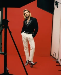 Bill Kaulitz wearing a black blazer and white trousers against a red studio backdrop, photographed by Julian Essink