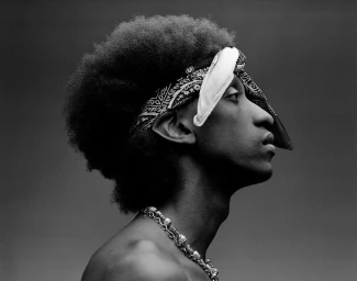 Profile portrait of a black man wearing a patterned bandana and silver chain necklaces against a dark background