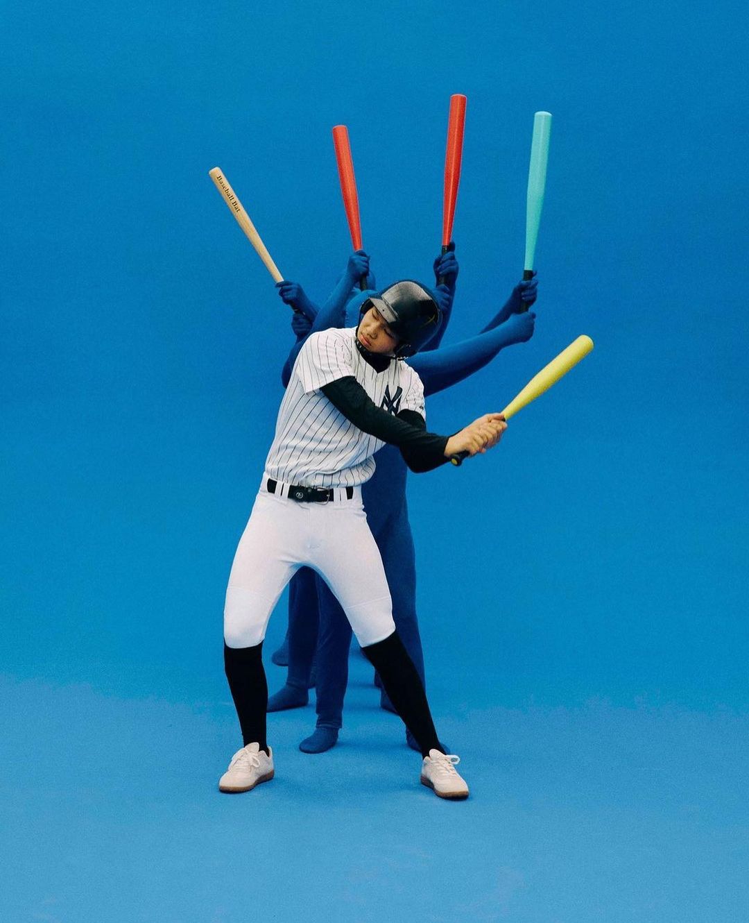 A baseball player in uniform swings a yellow bat, with blue-suited figures behind holding bats, all against a solid blue background.