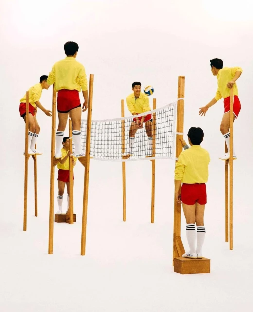 Several young men in yellow shirts and red shorts playing volleyball on stilts on a white background, creating a playful, dynamic composition.