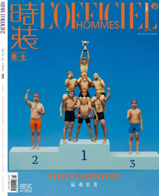 Men's fashion magazine cover featuring a pyramid of seven men wearing swimwear and medals, one holding a trophy on a blue background.