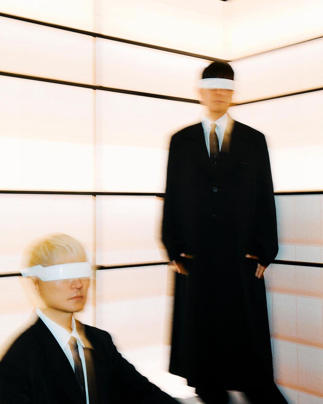 Two men in dark suits and white visors standing inside a brightly lit room with slatted walls.