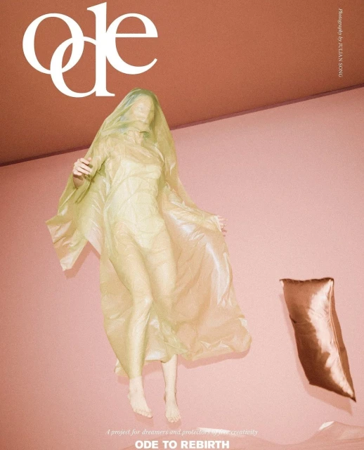 Person covered in sheer yellow material levitates in pink room next to floating pillow in conceptual fashion or editorial photograph.