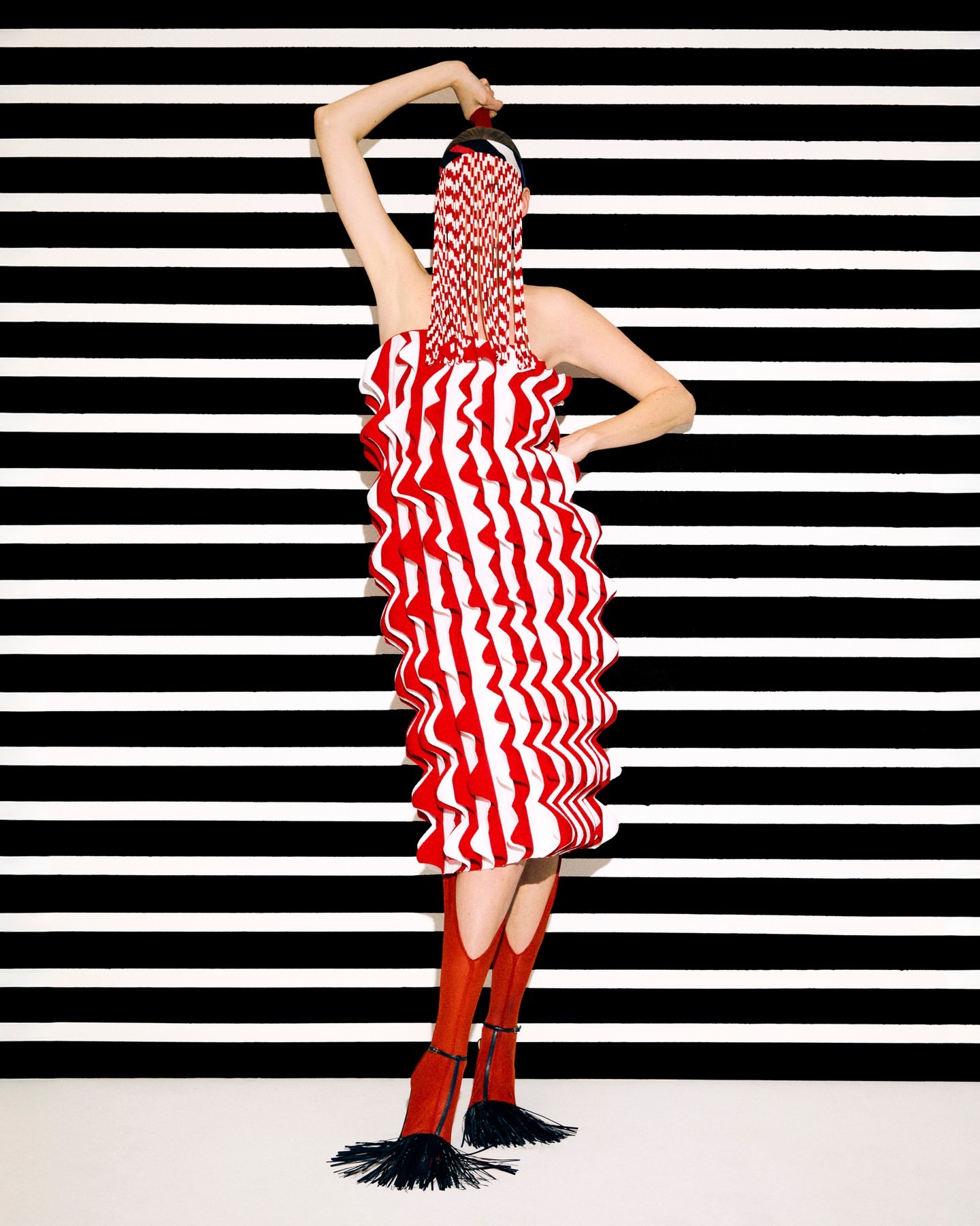 Woman in red and white striped dress and boots poses in front of black and white striped background in a fashion studio shot.