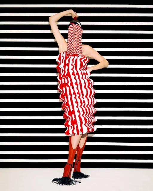 Woman in red and white striped dress and boots poses in front of black and white striped background in a fashion studio shot.