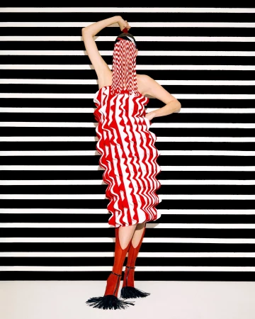 Woman in red and white striped dress and boots poses in front of black and white striped background in a fashion studio shot.