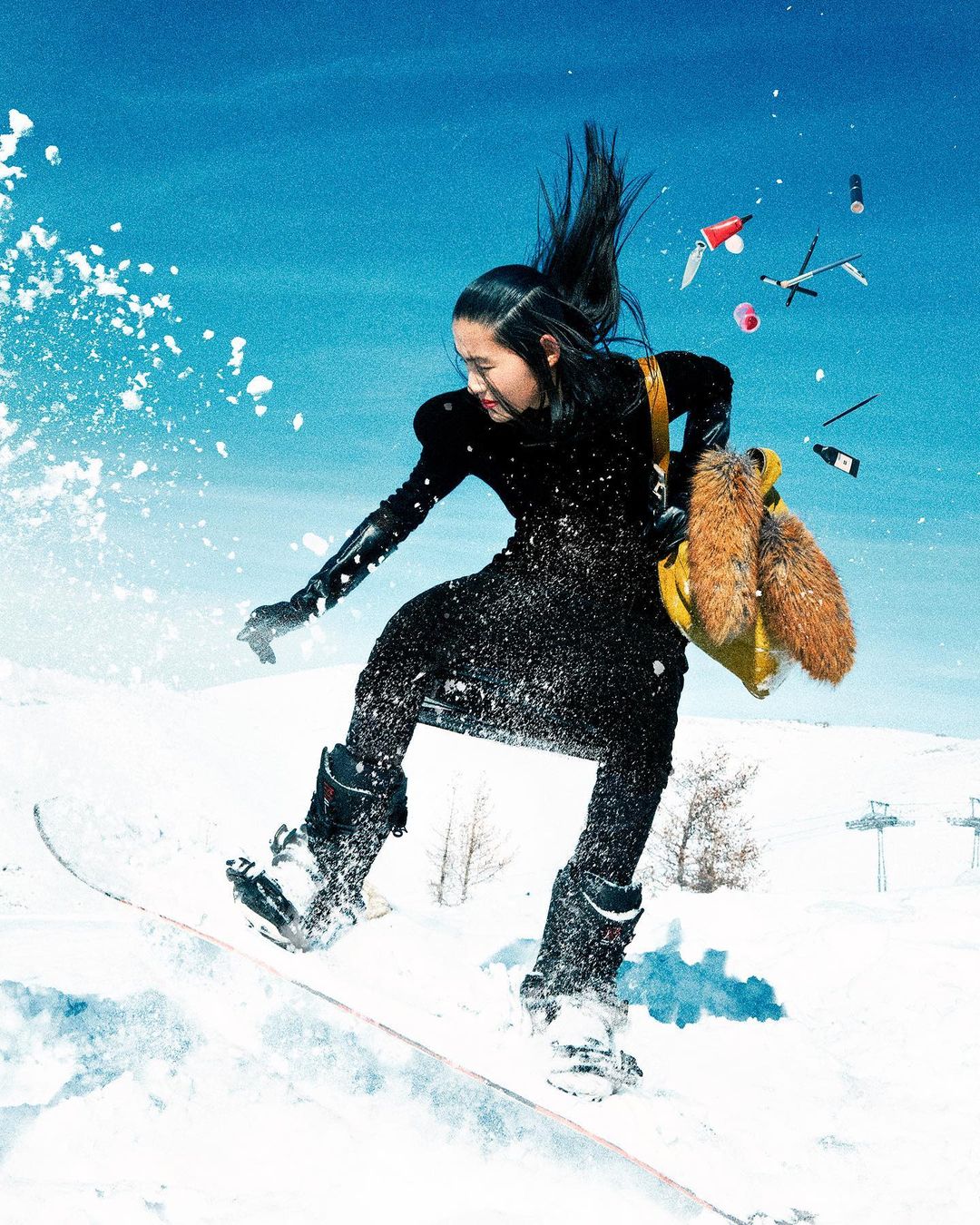 Woman in a black dress and boots is snowboarding on a snowy mountain with a blue sky and scattered accessories floating around her.