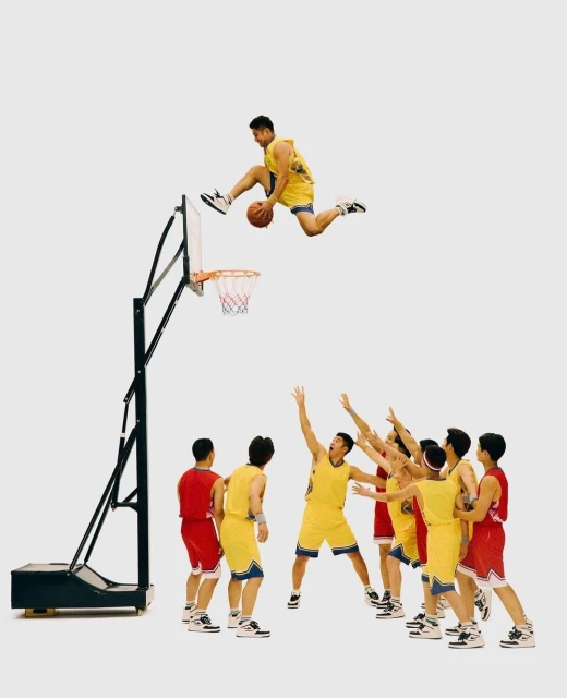 A basketball player leaps high above a basketball hoop, ball in hand, as his teammates watch him play on an indoor court in a sports event.