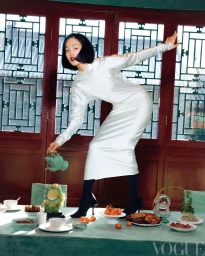 Woman in white satin dress standing on a dining table pouring tea from a green teapot in a traditional room