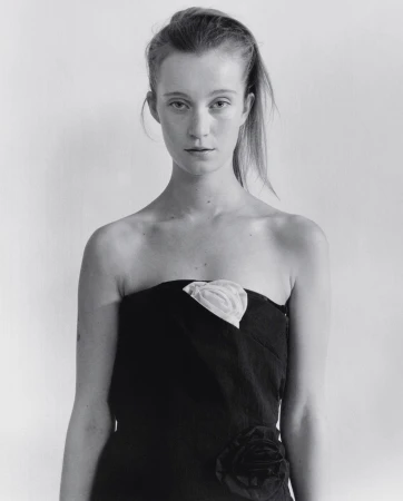 Monochrome portrait of a woman with long hair, wearing a strapless black dress with a white floral detail, against a white background.