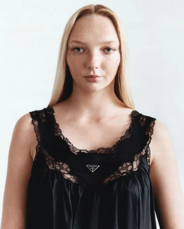 Close-up portrait of a fair-skinned young woman with blonde hair wearing a black lace-trimmed dress against a white background.