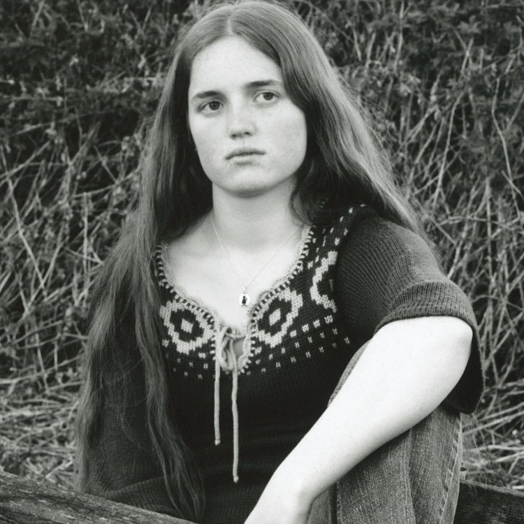 Monochrome portrait of a young adult woman with long brown hair wearing a patterned sweater in an outdoor setting.