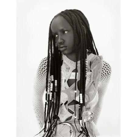 Black and white portrait of a Black woman with braided hair. She wears a light-colored, open-weave top and a belt, looking slightly away from camera.
