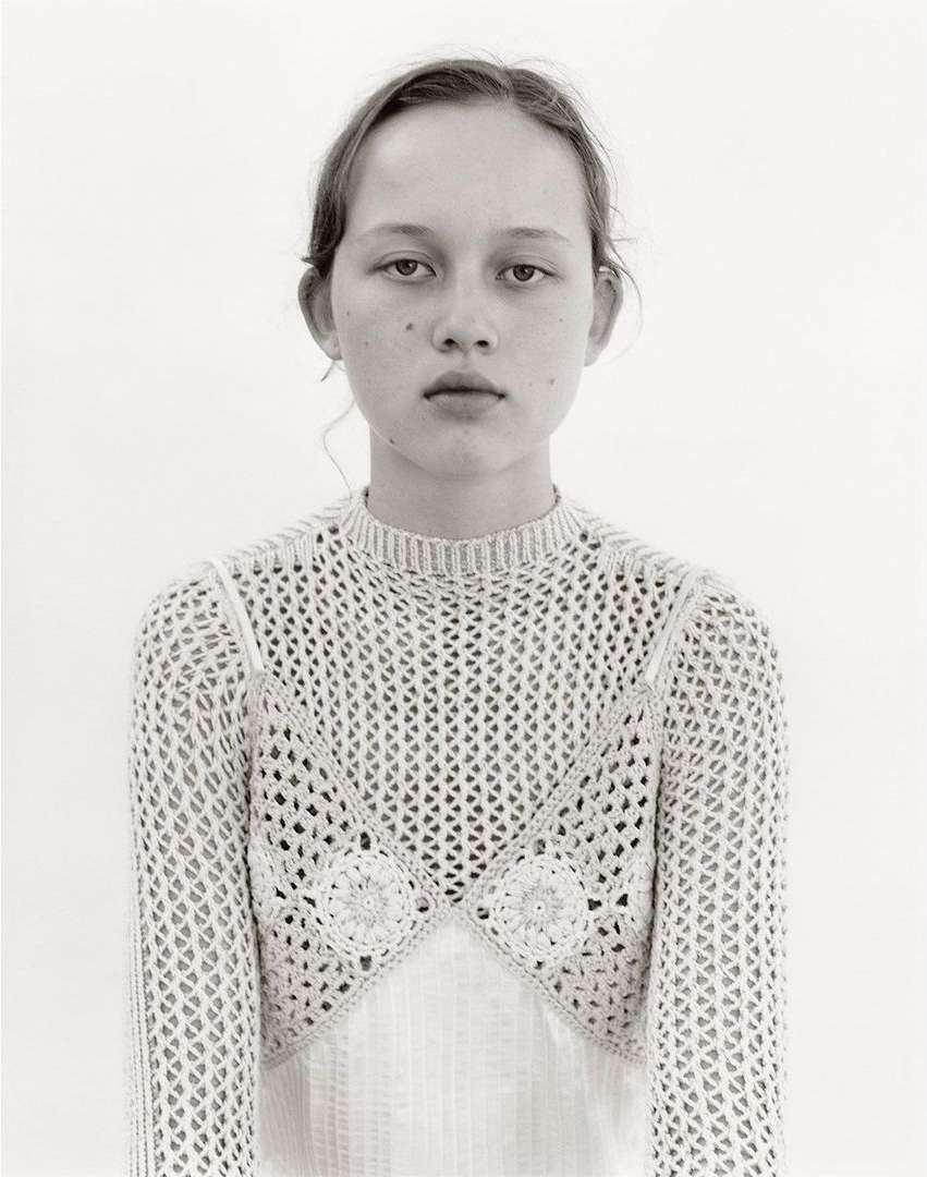 Portrait of a young woman wearing a textured crochet top against a plain white background