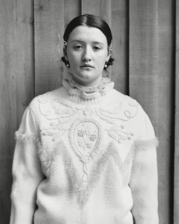 Monochrome portrait of a young woman wearing a textured white patterned sweater against vertical wooden planks