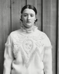 Monochrome portrait of a young woman wearing a textured white patterned sweater against vertical wooden planks
