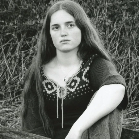 Monochrome portrait of a young woman with long dark hair wearing a patterned knit top against foliage