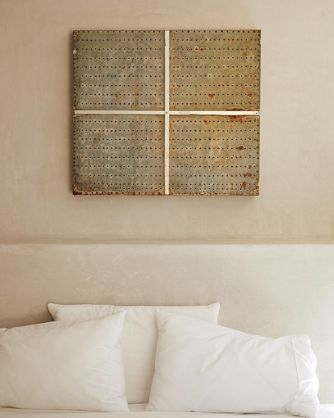 Bedroom interior with a bed featuring white linens and pillows, a unique metal headboard artwork with a minimalist aesthetic.
