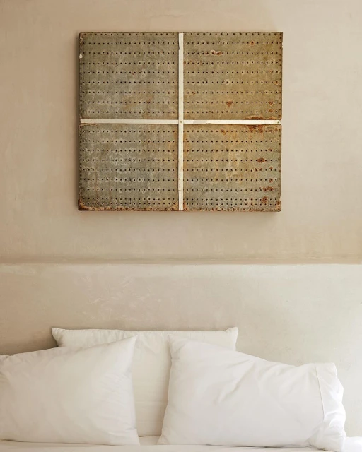 Bedroom interior with a bed featuring white linens and pillows, a unique metal headboard artwork with a minimalist aesthetic.