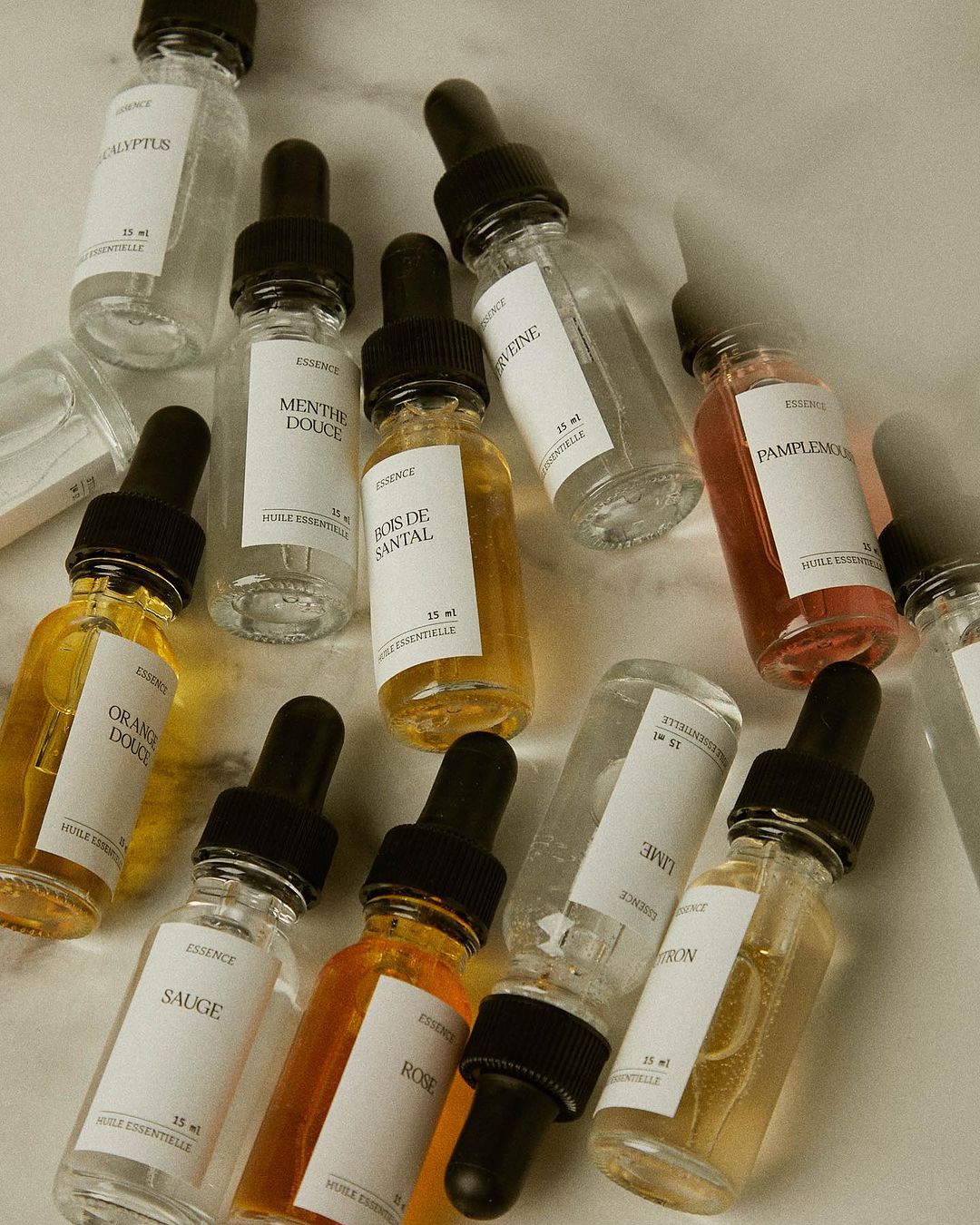 Overhead shot of several clear glass dropper bottles filled with various colored essential oils on a neutral surface.