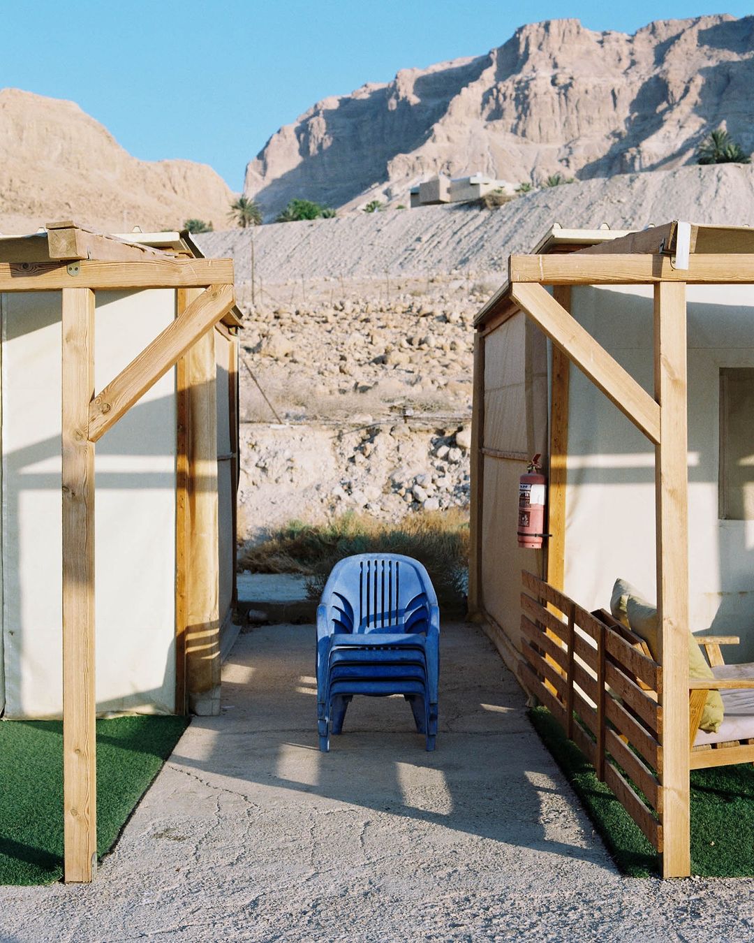 Stacked blue plastic chairs sit between two covered patio areas with a mountain background, creating a serene outdoor setting.